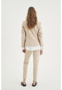 Blazer beige y pantalones ajustados, diseño a medida, material ligero, camisa blanca debajo y zapatos planos negros sencillos.