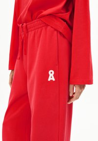 Rote Jogginghosen aus weichem Stoff mit einem Taillenband zum Schnüren und einem weißen Logodetail. Die Hose hat einen lockeren Schnitt mit weitem Bein.