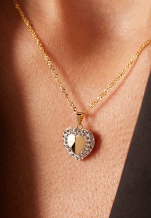 Collier en or avec une chaîne torsadée, featuring un pendentif en forme de cœur orné de cristaux transparents et d'un accent de cœur partagé en or au centre.