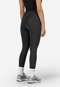 Melni augstie legingi, izgatavoti no elastīga materiāla, ar gludu tekstūru un šuvju detaļām, kopā ar sudraba sporta apaviem.