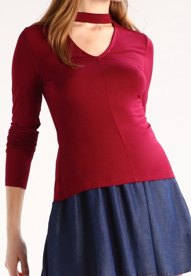 Atasan lengan panjang burgundy dengan leher V dan detail choker, memiliki desain yang fitted dan tekstur yang halus. Dipadukan dengan rok denim.
