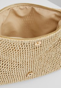 Beżowa pleciona torebka kopertowa z złotym zapięciem na zatrzask, rozpięta, ukazująca gładką beżową podszewkę.