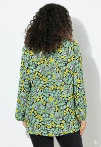 Blusa floreale con sfondo nero e motivi verdi, gialli e bianchi. Maniche lunghe e design dal taglio rilassato.
