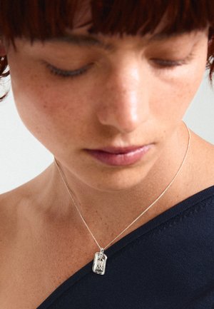 Collana con pendente in argento, dotata di un ciondolo rettangolare con un intricato design inciso, sospeso su una catena sottile e delicata.