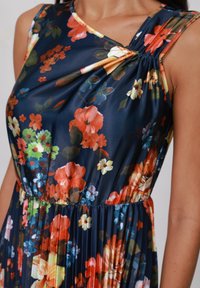 Rochie florală cu un fundal navy închis, flori vibrante multicolore, decolteu rotund și detaliu cu talie strânsă. Material ușor și neted.