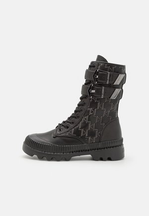 Botte de combat montante noire avec fermeture à lacets à l'avant, deux brides à boucles, panneau latéral à motifs et semelle épaisse à rainures.