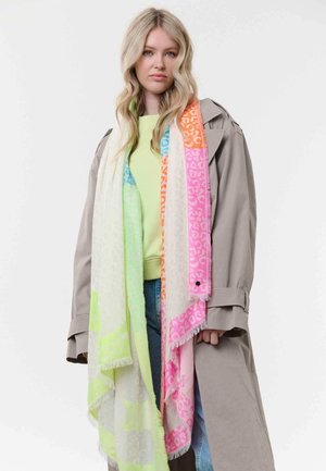 Young woman with long blonde hair wears beige trench coat, light green top, blue jeans, and long multicolored leopard-print scarf.