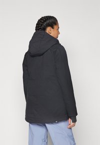 Black quilted puffer jacket with a hood, featuring a textured finish and elasticized cuffs, seen from the back.