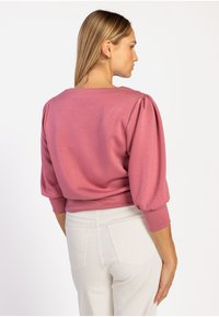 Roze pullover met pofmouwen, ronde halslijn en zachte stof. Gekleed met witte broeken, die een gladde textuur en getailleerd ontwerp tonen.