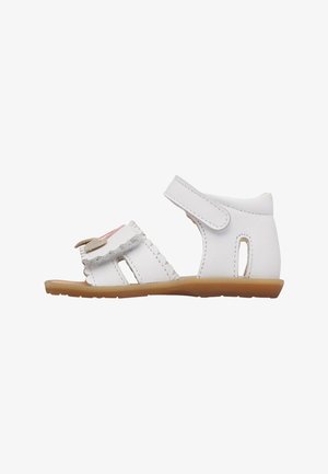 Sandalo bianco per bambino piccolo con chiusure a strappo in Velcro, bordi smerlati e un piccolo fiocco decorativo sul davanti, con suola piatta in gomma color beige.