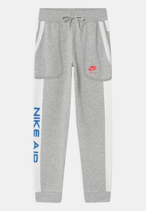 Harmaat collegehousut, jotka on valmistettu pehmeästä kankaasta, punainen Nike-logo, valkoiset sivuraitat ja sininen "NIKE AID" -teksti vasemmassa jalassa.