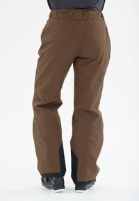 Bruine outdoorbroek met een rechte snit, voorzien van zwarte accenten bij de enkels en een logo op de tailleband. Gemaakt van een flexibele, weerbestendige stof.