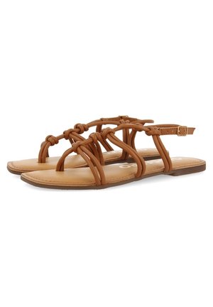 Sandales plates marron avec des brides en cuir nouées et une fermeture à boucle réglable à la cheville sur fond blanc uni.