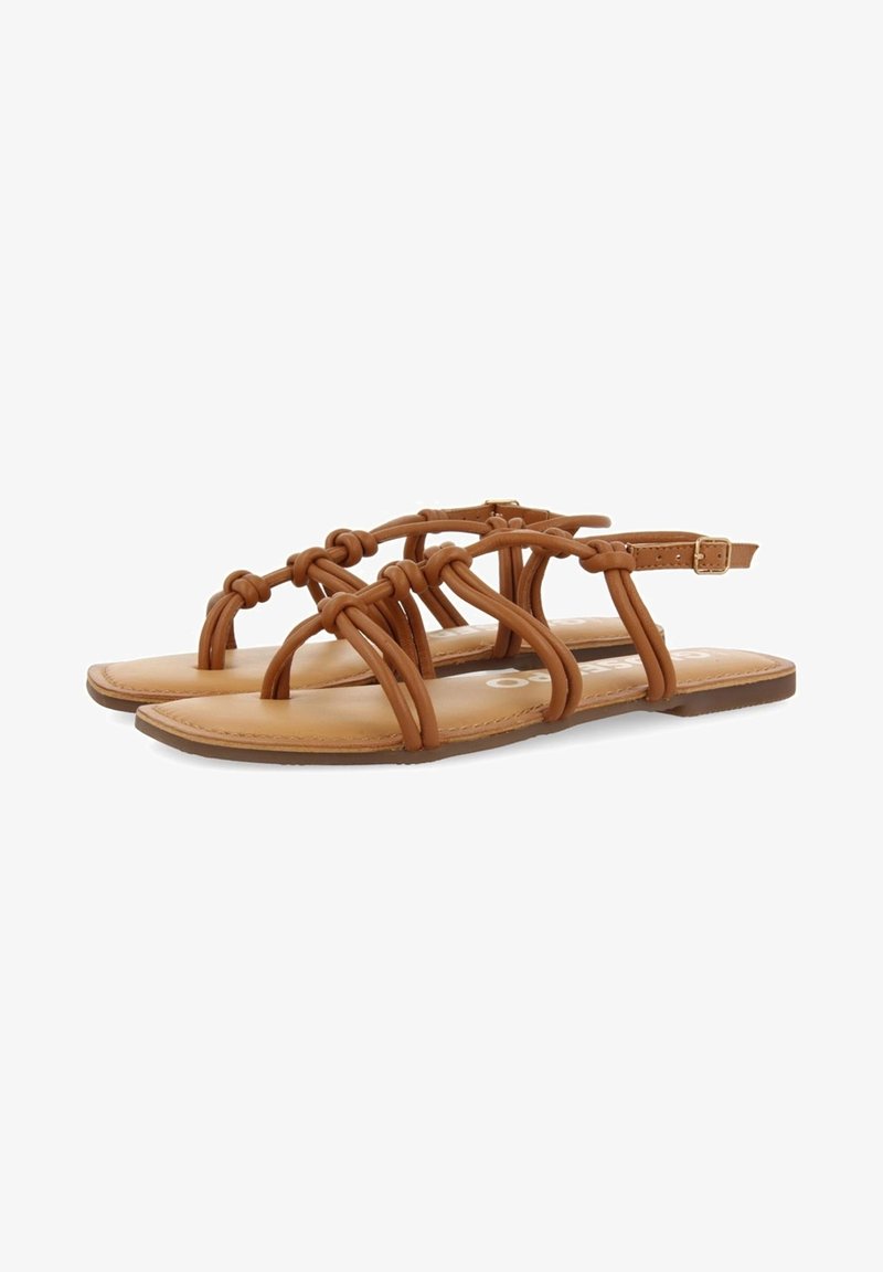 Sandales plates marron avec des brides en cuir nouées et une fermeture à boucle réglable à la cheville sur fond blanc uni.