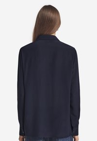 Granatowa koszula z długim rękawem uszyta z gładkiego materiału, z klasycznym kołnierzykiem, zapinanymi mankietami i luźnym krojem, pokazana z tyłu.