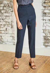 Pantalon bleu marine sur mesure avec une taille haute, un devant plat et des poches latérales. Associé à des sandales marron à talons avec un accent de boucle.
