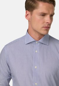 Srajca z gumbki v modro-belih navpičnih črtah. Bombažna tkanina z gladko teksturo. Ima razprto ovratnik in bele gumbe.