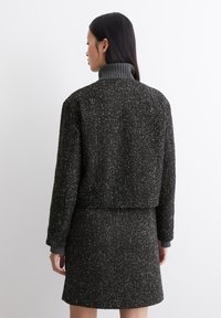 Schwarze Tweedjacke mit tailliertem Design, Fischgrätenmuster und grauem Rippkragen; kombiniert mit einem passenden Rock.