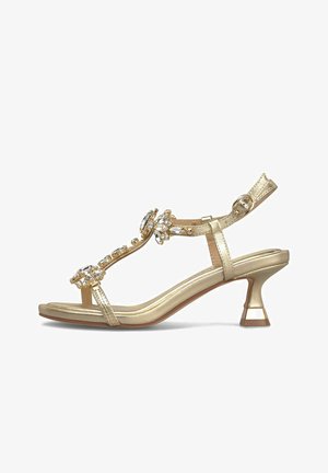 Złote sandały na wysokim obcasie z paskiem wokół kostki i klamrą, zdobione dekoracyjnymi przezroczystymi kamieniami ozdobnymi na pasku typu T.