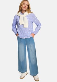 Chemise boutonnée bleu et blanc à pois, ourlet festonné, associée à un jean large bleu clair et des baskets blanches avec des accents caramel.