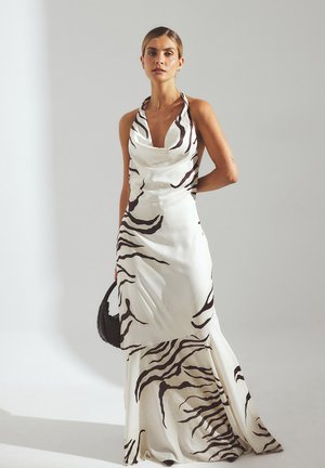 Donna che indossa un vestito bianco a collo alto con strisce abstract a zebra nere, mentre tiene una borsa a tracolla black intrecciata, in piedi contro uno sfondo neutro.