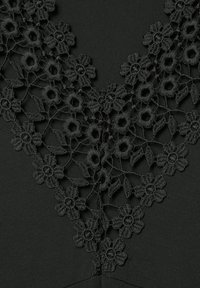 Schwarzer Stoff mit floralen Spitze-Details am Ausschnitt, featuring filigrane Blütenmuster und gewellte Kanten. Glatte Textur, elegantes Design.