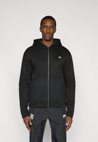 Μαύρη φούτερ ζακέτα με φερμουάρ, κατασκευασμένη από βαμβακερό μείγμα, με υφασμένη μπροστινή τσέπη, κουκούλα με κορδόνια και μικρό λογότυπο στο στήθος.