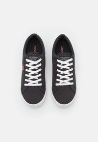 Zapatillas bajas de lona negra con cordones blancos y suela de goma. Presentan el logo de Levi's en la lengüeta y una etiqueta roja en el lado. Textura suave.