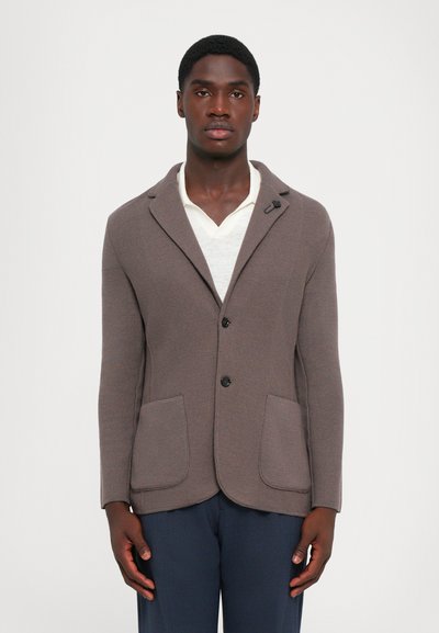 Blazer texturé marron avec un col cranté, deux poches avant, fermeture à un bouton et une doublure intérieure lisse porté sur une chemise crème.