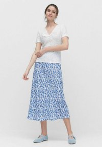 Hvid blonde kortærmet top kombineret med en blå blomsterprint maxi-nederdel. Nederdelen har et flydende design og suppleres med lyseblå slip-on sko.