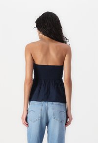 Marineblå topp uten stropper med smocket liv og flytende stoff. Kombinert med lyseblå denimjeans med baklommer og en løs passform.