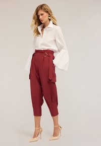 Chemise blanche à boutons avec des manches larges et fluides, associée à un pantalon bordeaux taille haute et effilé, avec des poches latérales et des passants de ceinture.