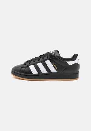 Baskets Adidas Campus noires avec des bandes blanches, semelle en gomme, lacets noirs et languette de talon blanche.