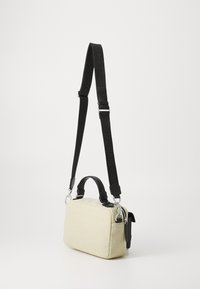 Canvas handbag in light beige with black leather accents. Features a detachable strap, zip closure, and dual top handles. Compact and rectangular design.