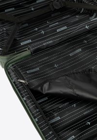 Otevřený tmavě zelený kufr s černým vzorovaným podšívkou, na které jsou letadla, obsahující zipy, elastické popruhy a síťové přihrádky pro organizované balení.