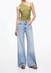 Haut asymétrique texturé couleur vert olive associé à un jean bleu clair à jambes larges. Le jean comporte un ourlet effiloché et des poches avant.