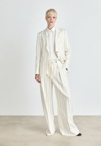 Wit gestreept pak met een blazer met één knoop en broek met trekkoord. De stof heeft een gladde textuur, aangevuld met een frisse witte overhemd.