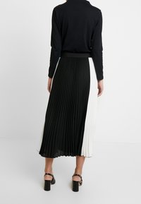 Zwart-wit geplooide rok met contrasterende kleuren, elastische tailleband en vloeiende textuur, gecombineerd met sandaalhakken.