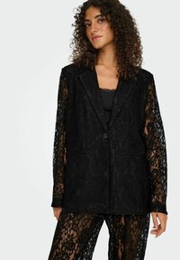 Črni čipkasti blazer s prilagojeno zasnovo, z dolgimi rokavi, sprednjimi žepi in zapenjanjem na en gumb, nošen preko ujemajoče se majice.