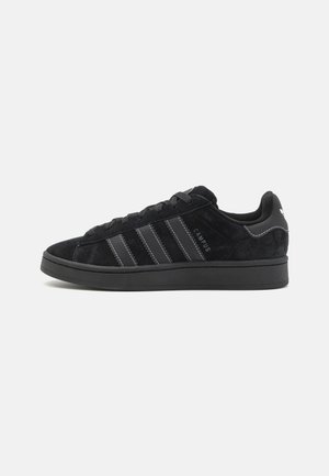 Zwarte Adidas Campus sneaker met zwarte leren strepen, suède bovenwerk, vetersluiting en merknaam op het hielstuk tegen een witte achtergrond.