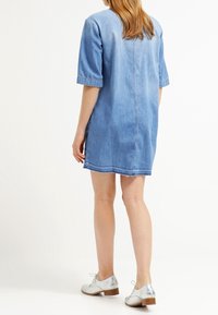 Denimmekko lyhyillä hihoilla, vaaleansininen pesu ja suora leikkaus. Mukana takasauma ja räikeä helma. Yhdistetty hopeisiin oxford-kengiksi.