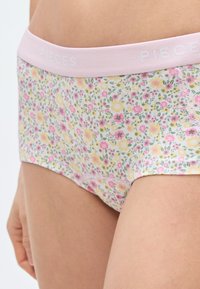 Moteriškos apatinės kelnaitės su gėlių raštu ir švelniu rožiniu juosmeniu, pažymėtu užrašu „PIECES“. Pagamintos iš lengvos medžiagos, puoštos pastelinės spalvos gėlėmis ir žaliais lapeliais.