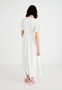 Witte, jurk tot de knie met korte, gerimpelde mouwen; heeft een oogjesstof, een aangesloten taille en een vloeiende rok. Draagt het met roze blokhak-sandalen.