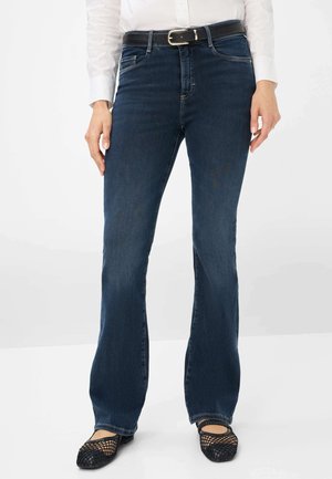Dunkelblaue Schlagjeans mit einer mittelhohen Taille, die über fünf Taschen und sichtbare Nähte verfügt. Ein schwarzer Gürtel mit einer silbernen Schnalle betont die Taille.
