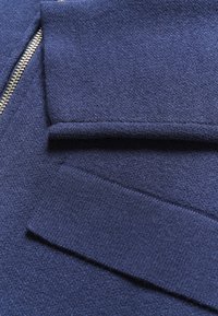 Marinblå zip-sweater med en strukturerad tyg. Har ribbade ärmslut. Slät yta med en tight passform. Direkt fokus på plaggets detaljer.