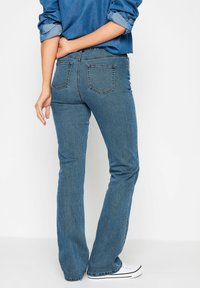 Jeans dżinsowe w fasonie dzwonów w średnim niebieskim kolorze o gładkiej fakturze. Posiadają standardowy pas, dwie tylne kieszenie i lekko elastyczny materiał.