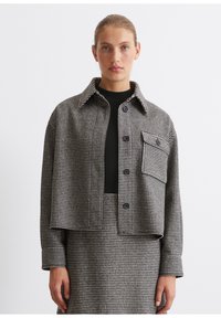 Checkered cropped jacket in black and white, featuring a collared neck, front buttons, and a single chest pocket. Textured woven fabric.