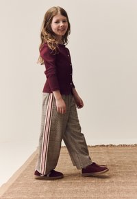Cardigan côtelé bordeaux avec boutons, associé à un pantalon large à carreaux avec des rayures roses, et des baskets bordeaux.
