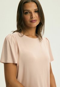 Koszulka z krótkim rękawem w jasnoróżowym kolorze, wykonana z miękkiej tkaniny, z okrągłym dekoltem i delikatnie bufowymi rękawami, oferująca luźny krój.
