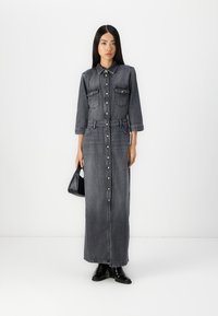 Mørk denim maxi skjortekjole med lange ermer, knappestolpe foran, brystlommer og belte i midjen. Kombinert med svarte tilbehør.